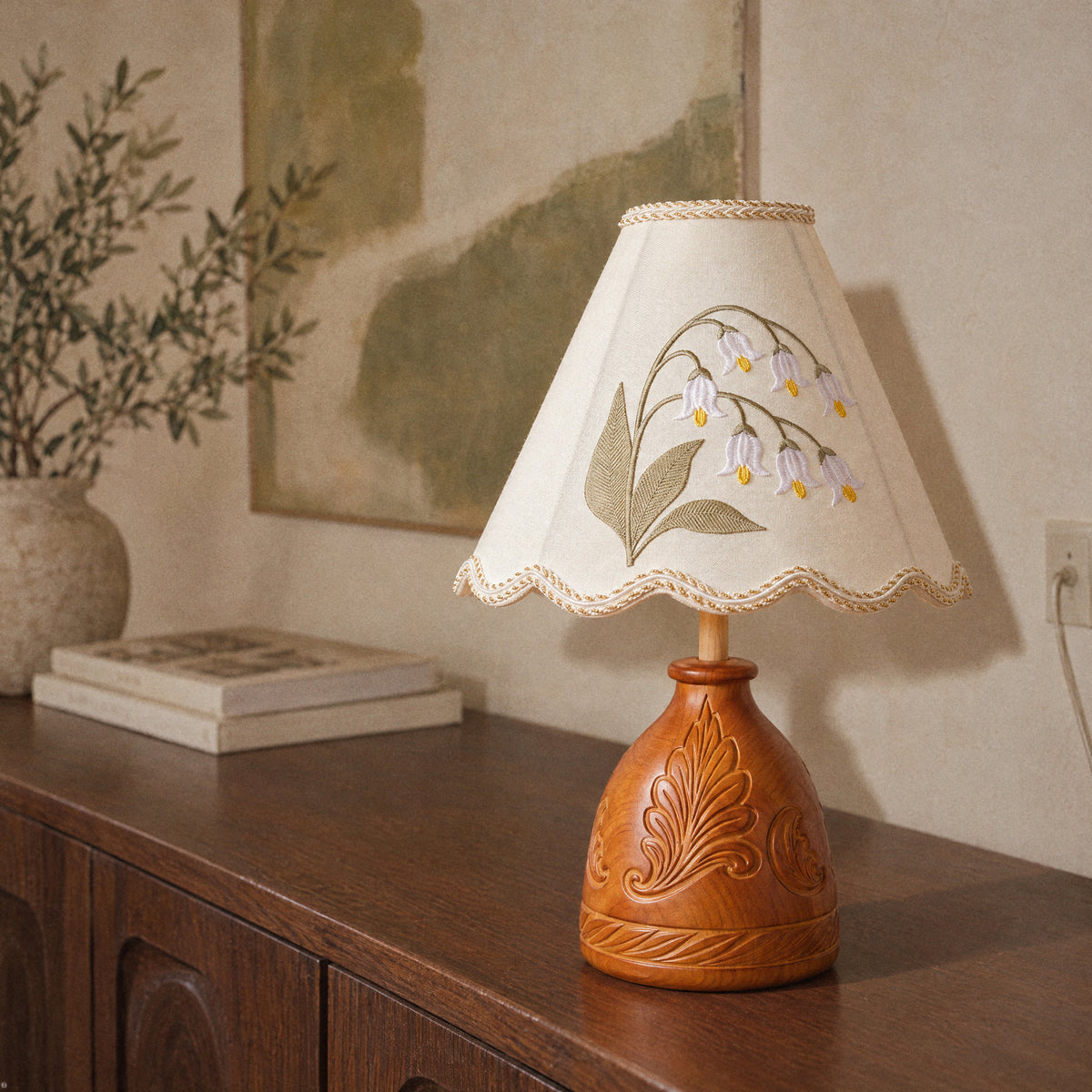 Close view of the carved reddish-amber ash wood base and the lower hem of the embroidered lamp shade