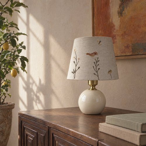 Cream ceramic table lamp with a bird and daisy embroidered shade in a room