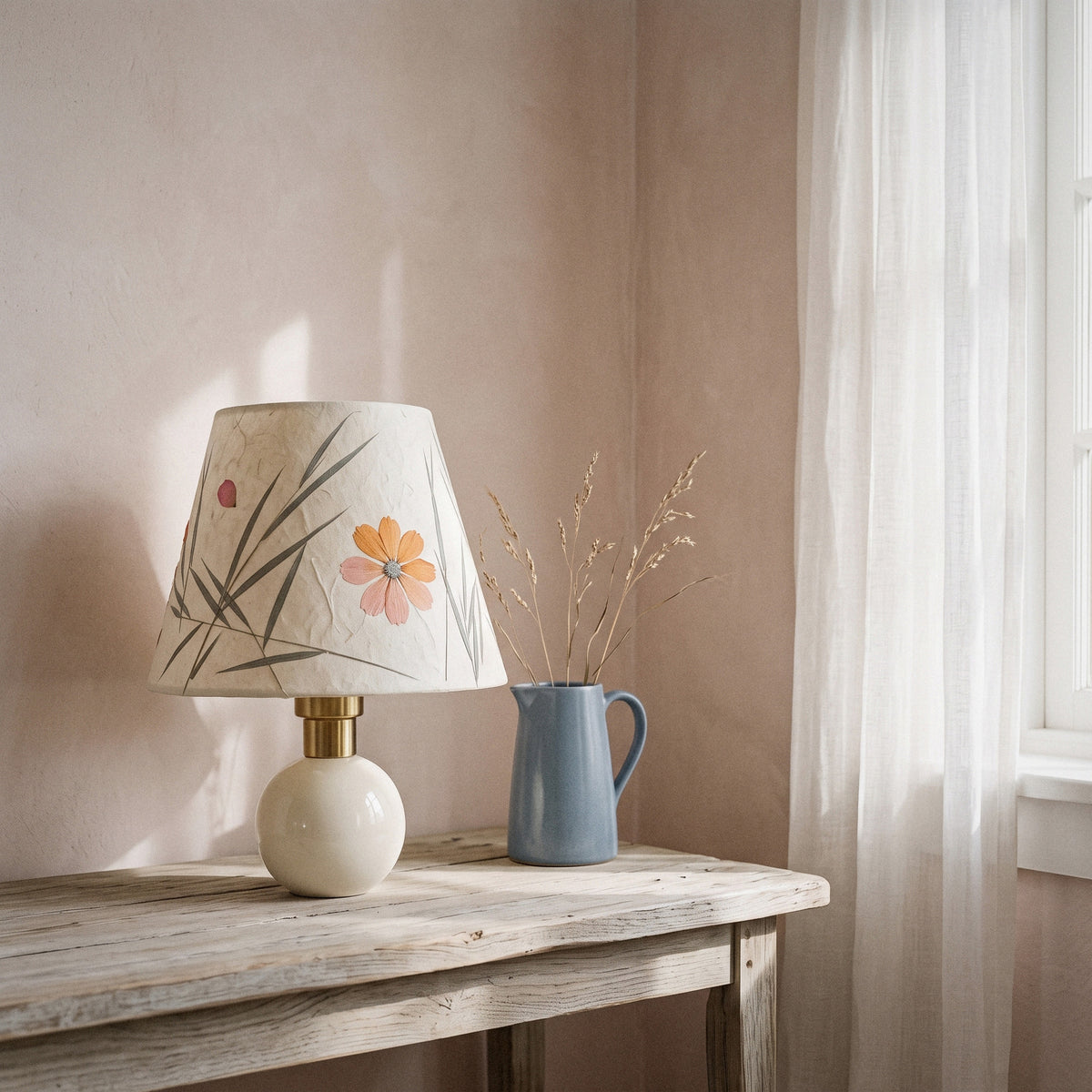 Cream ceramic table lamp with a pressed-flower and grass paper shade on a table in morning light