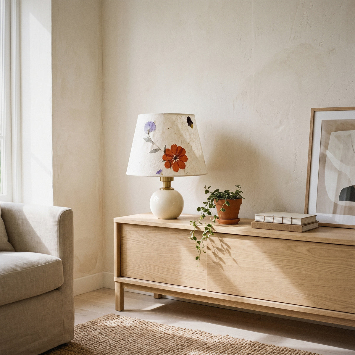 Cream ceramic table lamp with a pressed-flower paper shade on a sideboard beside an armchair and a rug