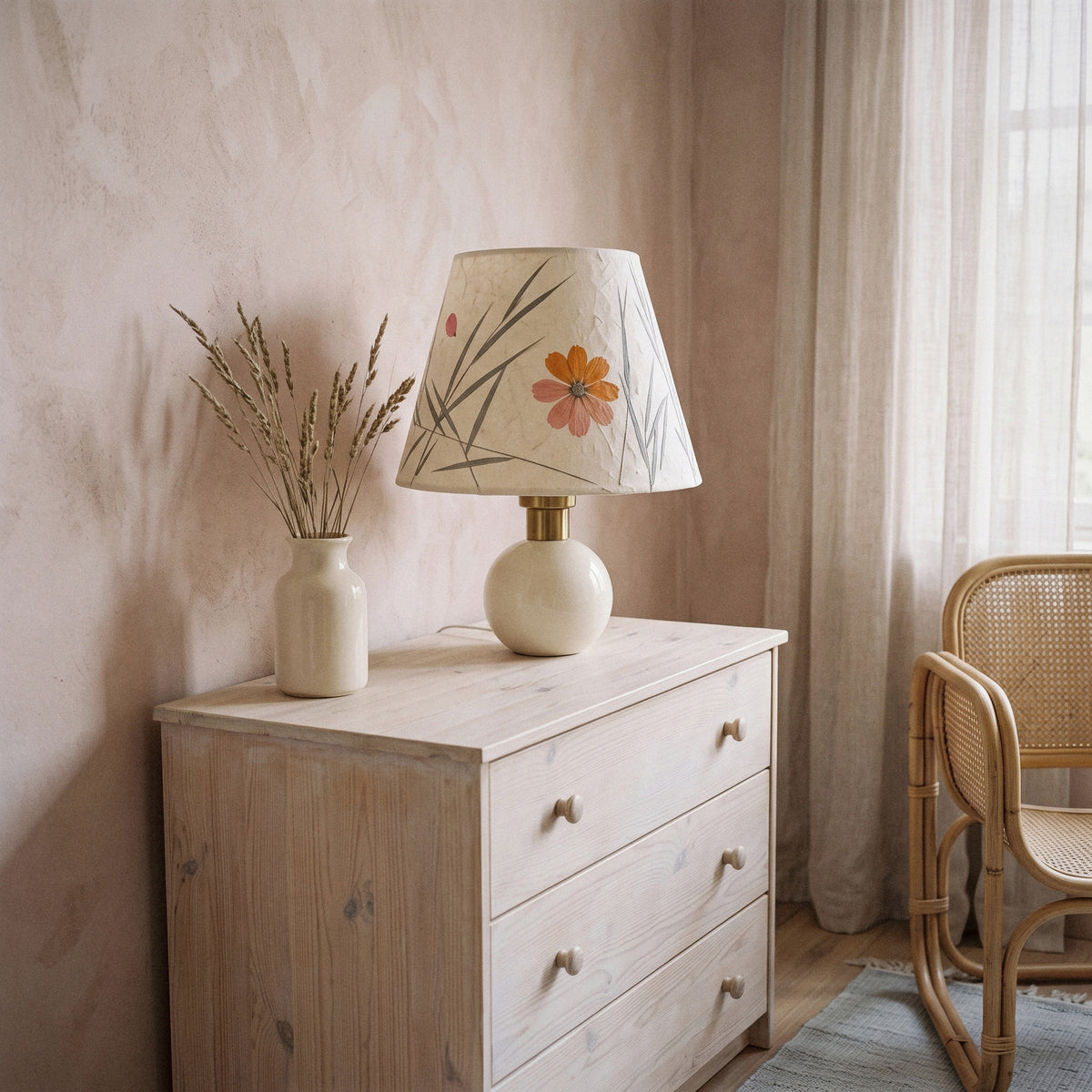 Cream ceramic table lamp with a pressed-flower and grass paper shade on a sunny dresser with rattan
