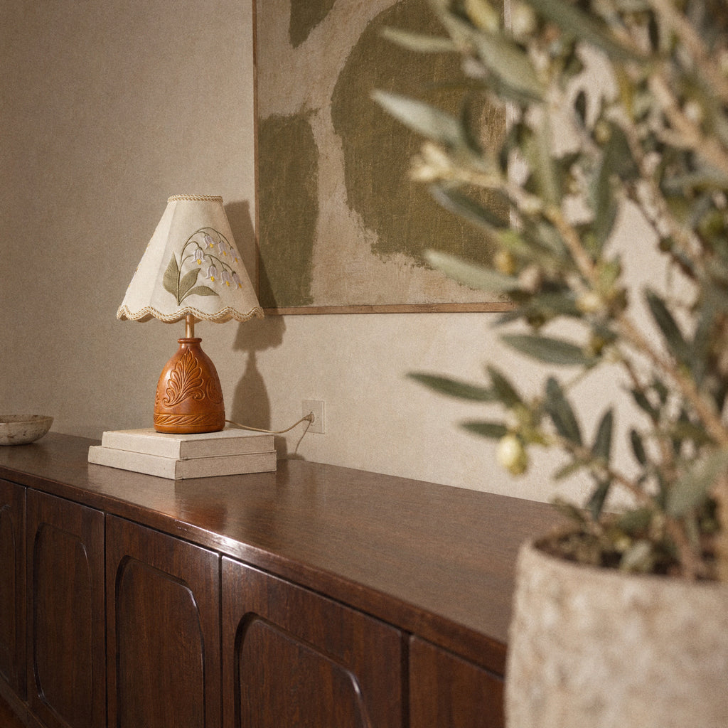 Lily of the Valley table lamp on a stack of books with an olive plant in the foreground