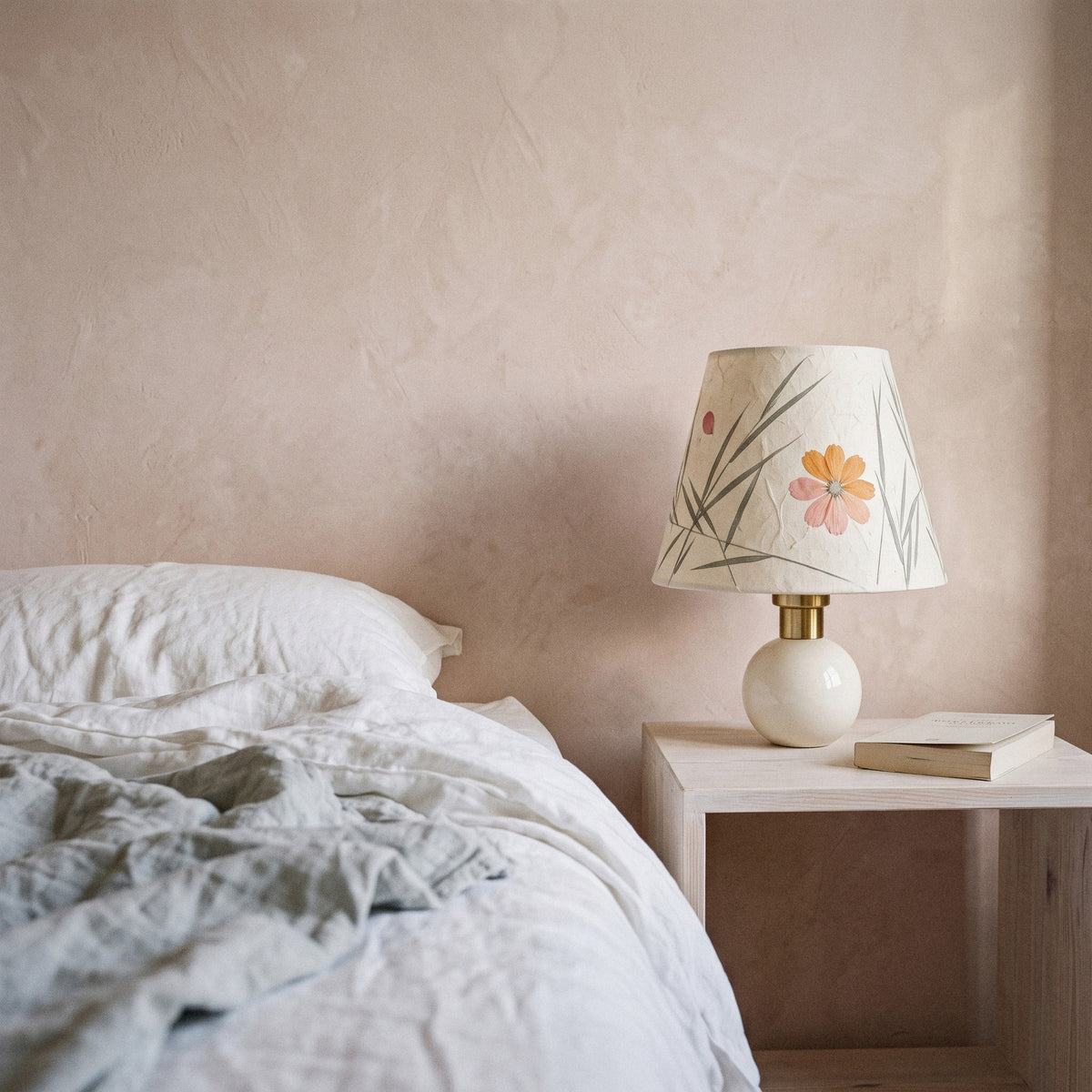 Cream ceramic table lamp with a pressed-flower and grass paper shade on a blush bedside table