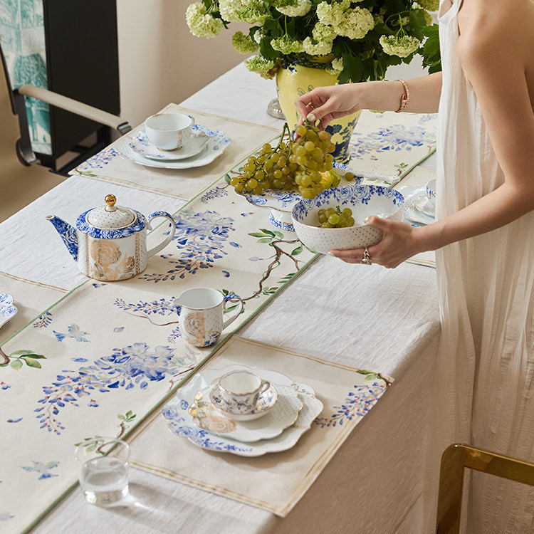 Woman setting a table with floral placemats and teacups.