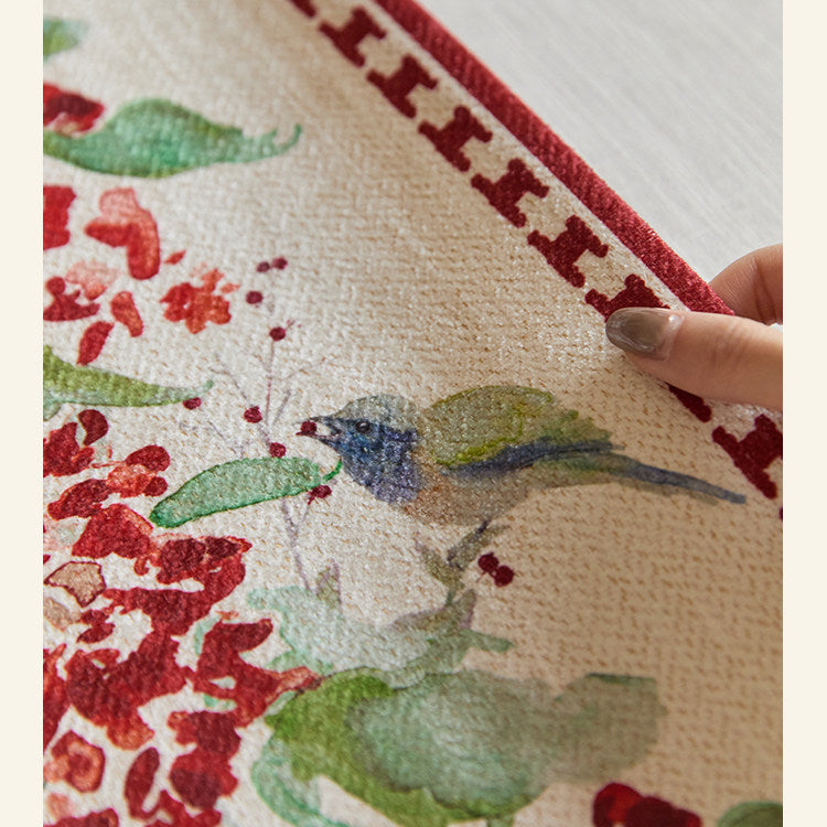Close-up of a fabric with floral and bird pattern held by a hand.