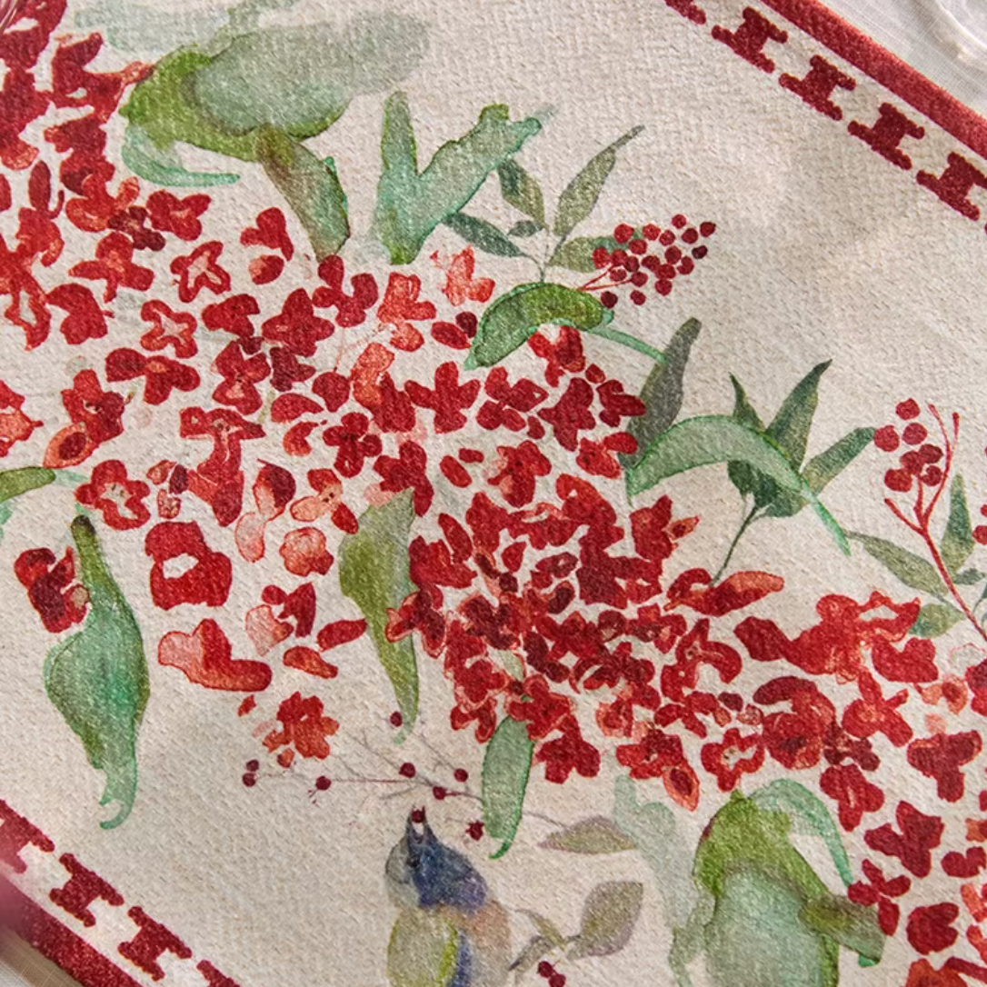 Decorative tablecloth with red floral pattern and green leaves on a white background