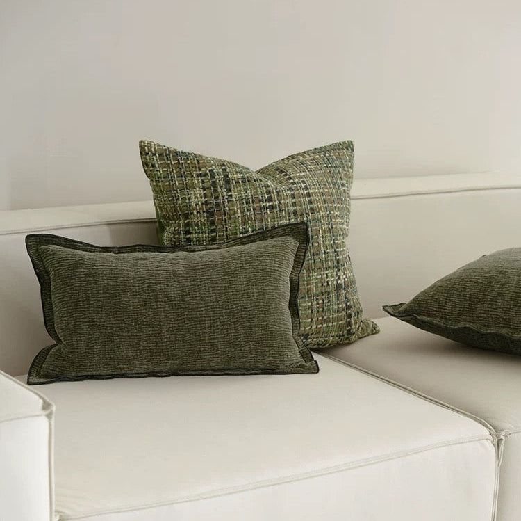 A set of square jacquard pillow covers with a green pattern and tassels, arranged on a white sofa.