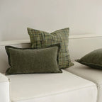 A set of square jacquard pillow covers with a green pattern and tassels, arranged on a white sofa.