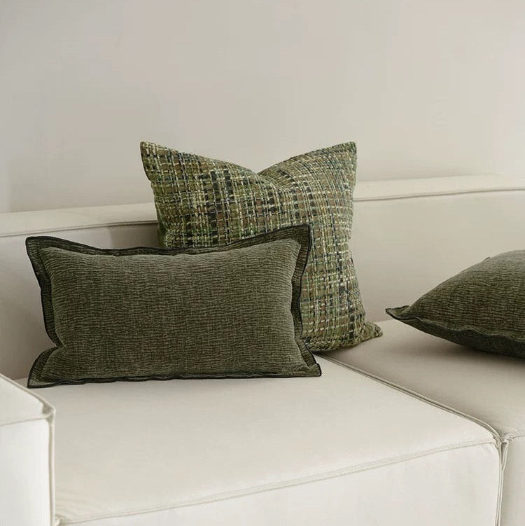A set of square jacquard pillow covers with a green pattern and tassels, arranged on a white sofa.