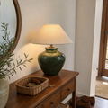 Green crackle-glaze ceramic table lamp with a wide linen shade, lit on a walnut entryway console beside a round mirror.
