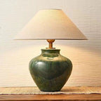 Front view of the green ceramic table lamp showing the mottled crackle glaze, wood neck and wide cream linen shade.