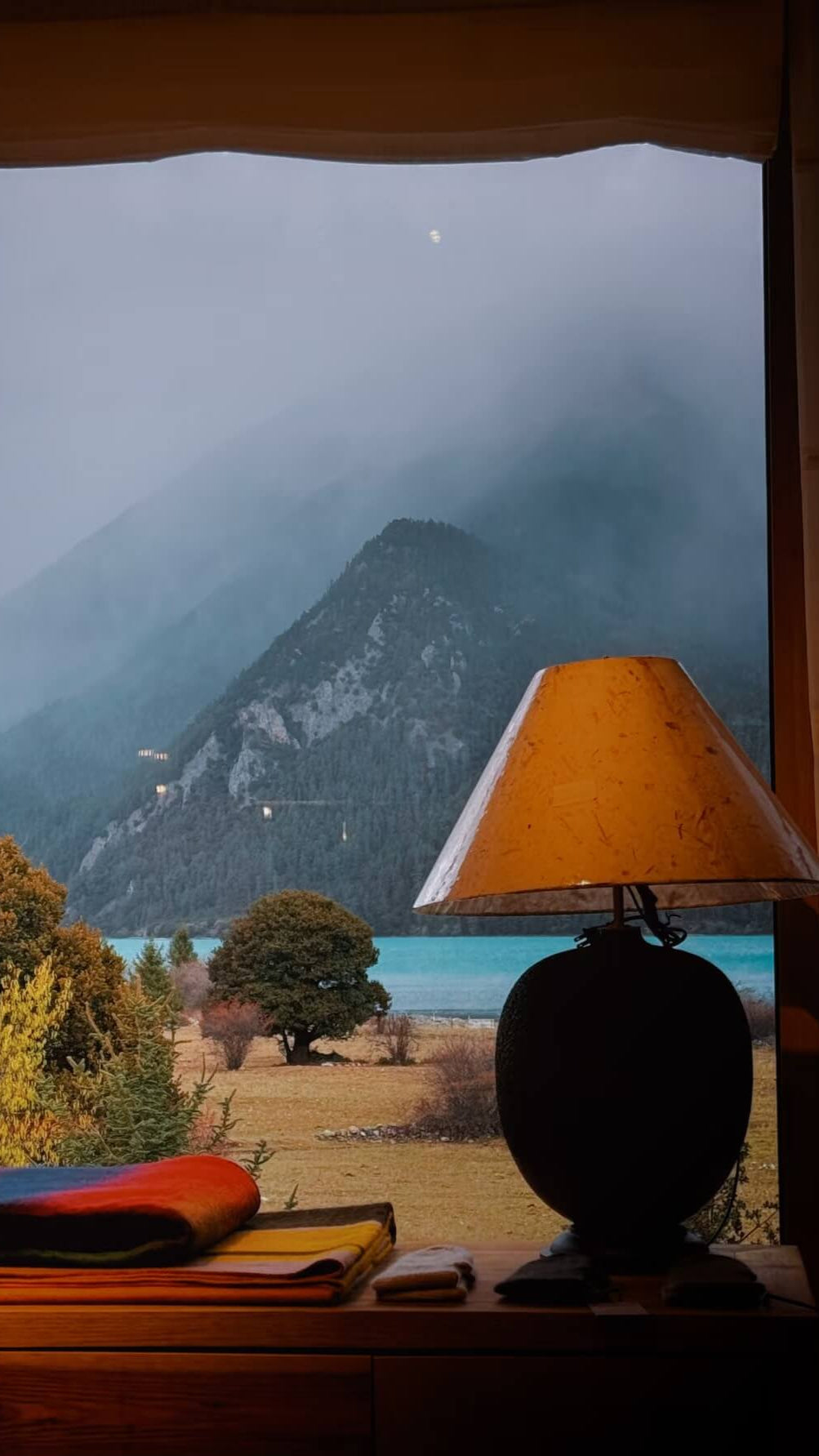 Lamp on a table with a scenic view of mountains and trees through a window.