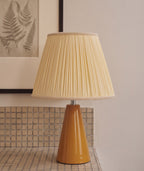 Close view of an amber glazed ceramic table lamp with a cream pleated shade on a tiled counter