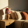 Handwoven rattan lamp with floral fabric shade placed beside bed, styled in a cozy daylight bedroom setting for a natural and elegant look.