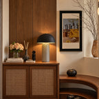 Black and white striped ceramic table lamp with a matte black dome shade, lit on a walnut cabinet with woven cane doors