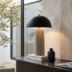 Mid-century modern dome table lamp in matte black with a black and white striped ceramic base, lit on a console by a window