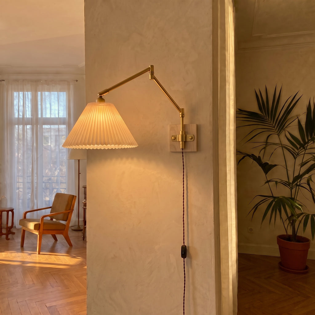 Plug-in swing arm wall sconce with a lit pleated shade on a plaster wall in a sunlit room with herringbone floors