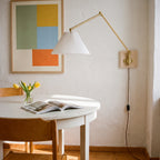 Swing arm wall sconce with a white pleated shade over a round dining table, a plug-in wall light for a small dining nook