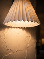 Close view of a lit pleated lamp shade on a wall sconce, warm light spreading over textured plaster