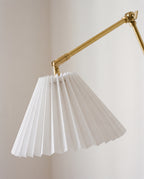Close view of a white pleated shade on a brass swing arm wall sconce, unlit against a pale wall