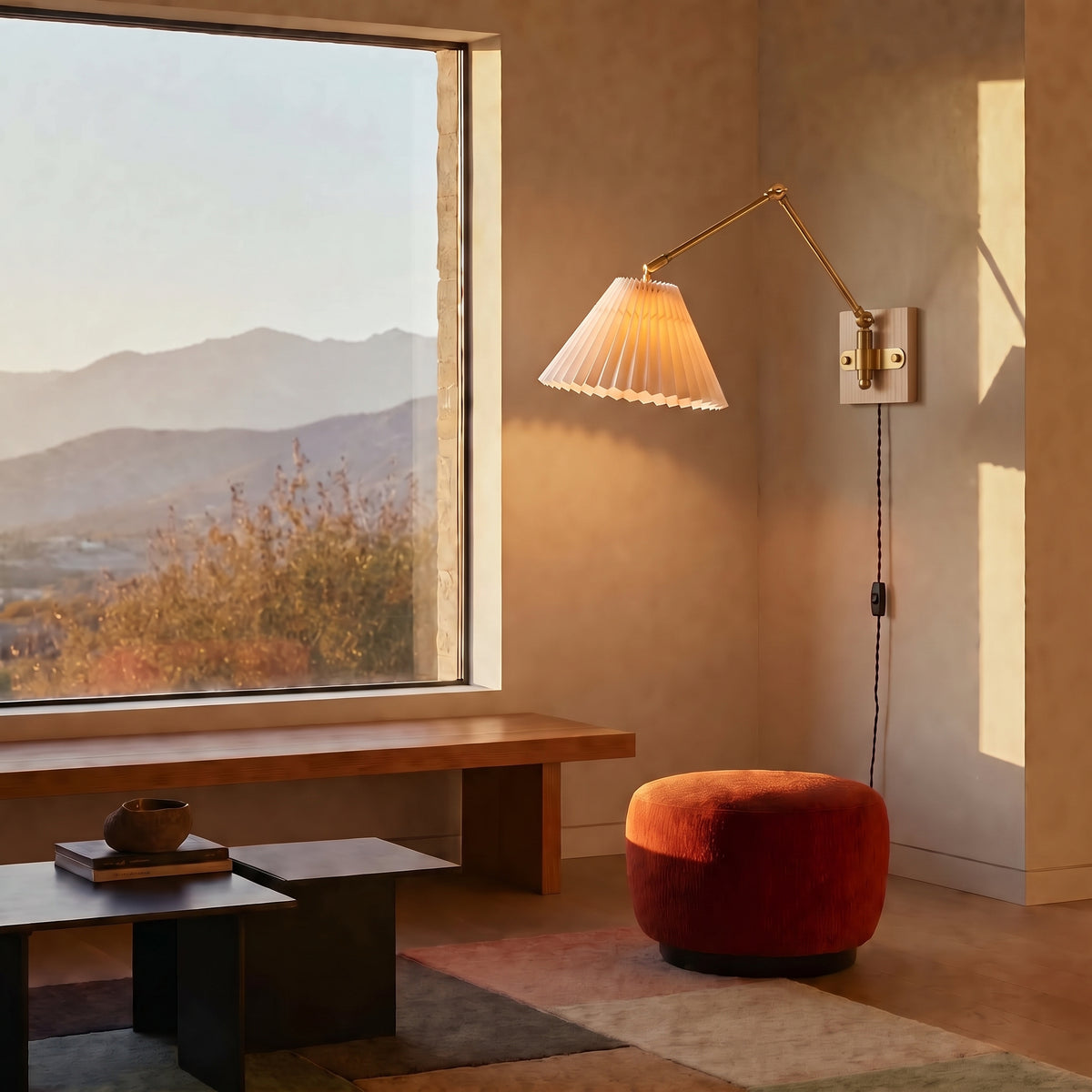Plug-in swing arm wall sconce with a pleated shade in a living room with a mountain view, a bench and a rust-orange pouf