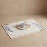 Teacup and saucer on a decorative placemat with floral patterns on a beige background