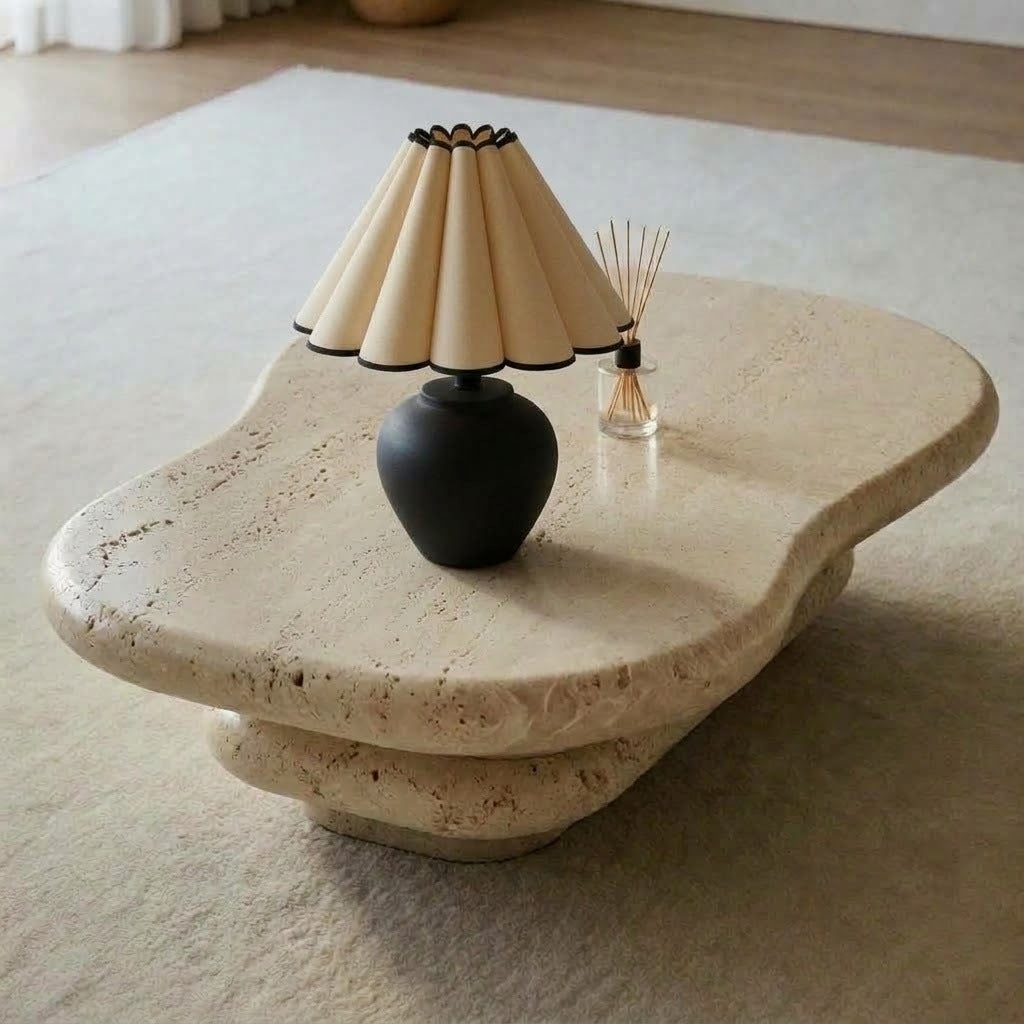 Matte black round-bellied lamp with a cream petal pleated shade on a free-form travertine table beside a reed diffuser