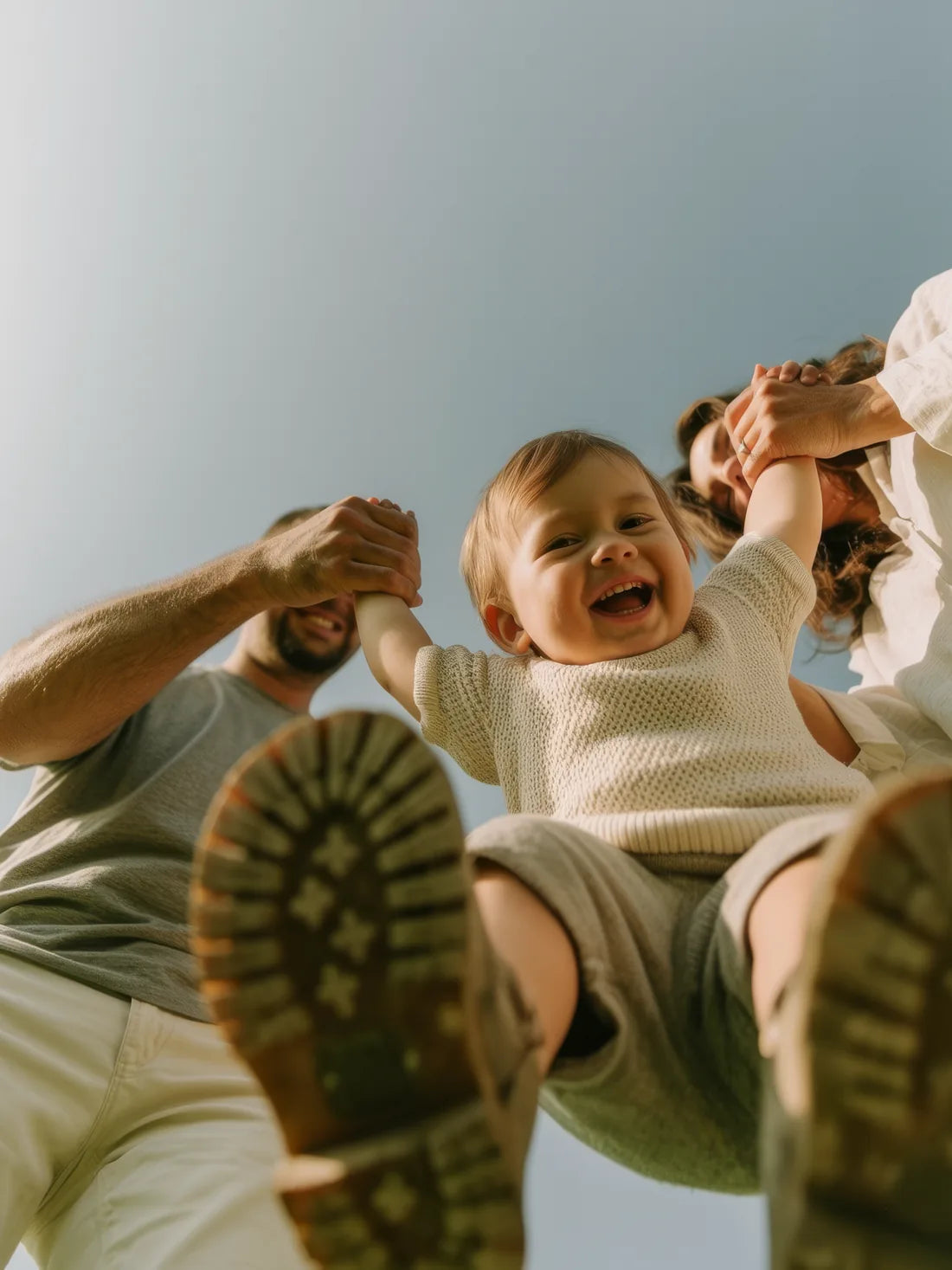 A laughing toddler swung between his parents, seen from below