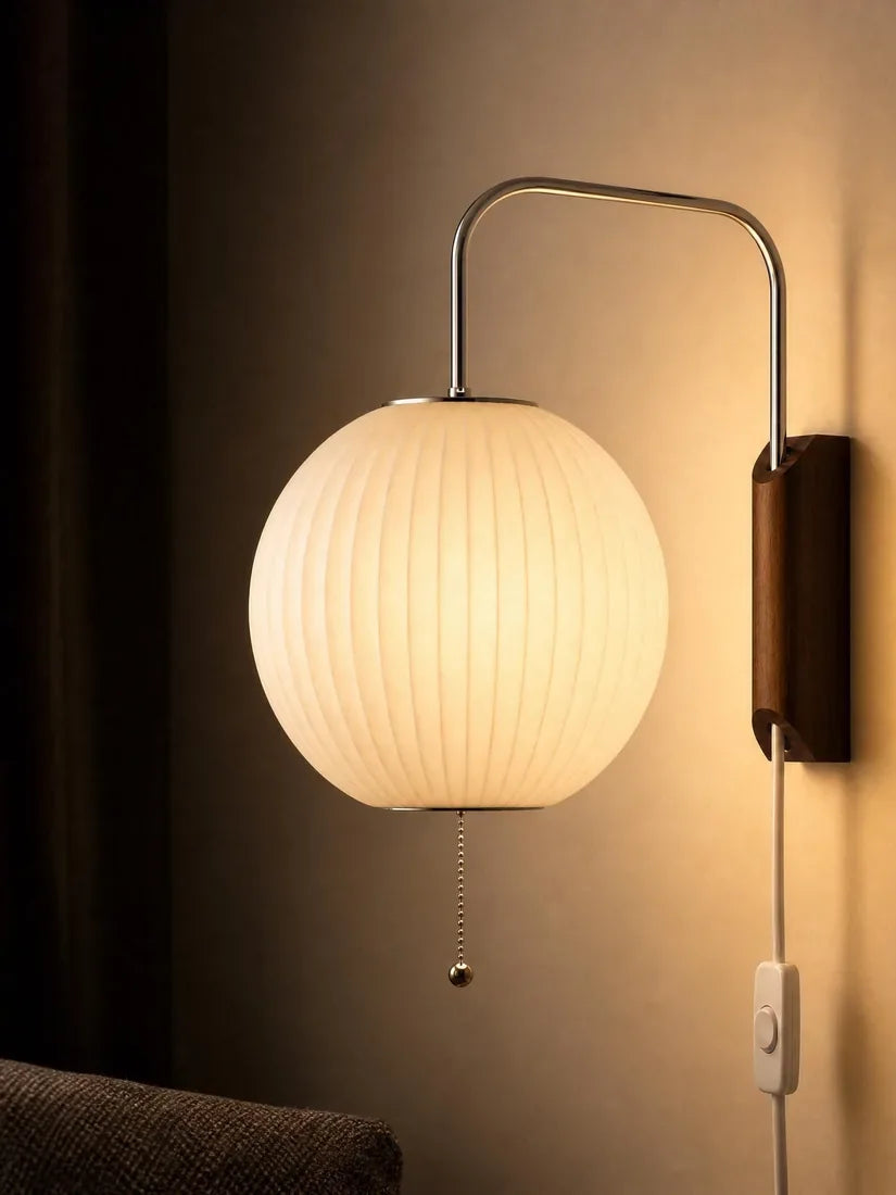 A globe wall sconce lit against a warm dark wall beside a framed print